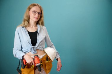 Koruyucu kasklı genç bir kadın işçi arka planda izole edilmiş bir ev planı tutuyor. Güzel gülümseyen beyaz kadın mimar yeni bir proje planlıyor. İnsanlar mimarlık projesinde çalışıyor