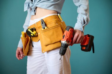 Arka planda elektrikli tornavida tutan kemerli genç bir bayan işçi. Yeni bir proje planlayan beyaz bir kadın. Stüdyoda portre.