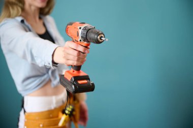 Arka planda elektrikli tornavida tutan kemerli genç bir bayan işçi. Yeni bir proje planlayan beyaz bir kadın. Stüdyoda portre.