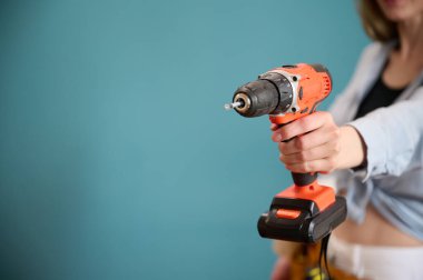 Arka planda elektrikli tornavida tutan kemerli genç bir bayan işçi. Yeni bir proje planlayan beyaz bir kadın. Stüdyoda portre.