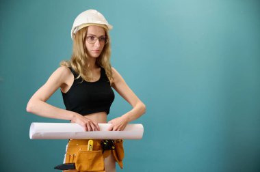 Koruyucu kasklı genç bir mimar kız arka planda izole edilmiş bir ev planı tutuyor. Güzel beyaz kadın mimar yeni bir proje planlıyor. İnsanlar mimarlık projesinde çalışıyor
