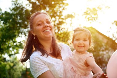 Anne ve kızı bahçede oynuyorlardı. Güzel bir aile dışarıda poz veriyor. Yaz manzarasında küçük mutlu bir kız. Tatlı küçük çocuk dışarıda.