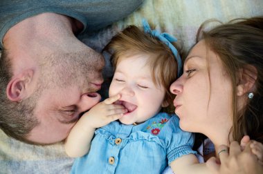 Avluda çocuklarıyla oynayan ebeveynlerin yakın çekim görüntüsü. Sevgi dolu bir aile, sevgi dolu ebeveynler tarafından desteklenen bir bebeğe sarılıp öper. Elbise giymiş sevimli küçük bir kızın kesilmiş portresi..