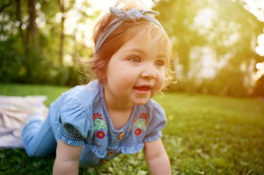 Bahçedeki çimlerin üzerinde sevimli bir kız. Portreyi kapat. Yaz manzarasında küçük mutlu bir kız. Tatlı küçük çocuk dışarıda.