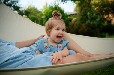 Anne ve kızı bahçede oynuyorlar, hamakta yatıyorlar. Güzel bir aile dışarıda poz veriyor. Yaz manzarasında küçük mutlu bir kız. Tatlı küçük çocuk dışarıda.