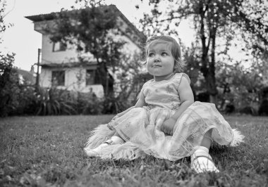 Bahçedeki çimlerin üzerinde sevimli bir kız. Portreyi kapat. Yaz manzarasında küçük mutlu bir kız. Tatlı küçük çocuk dışarıda.