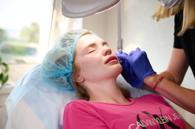 Kozmetik uzmanı hastanın yüzüne cerrahi olmayan düzeltmeler yapmak için madde enjekte ediyor. Doldurucu iğneler. Estetik tedavi konsepti. Ivano-frankivsk, Ukrayna - 08 / 17 / 2023