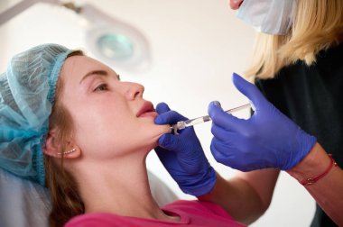 Kozmetik uzmanı hastanın yüzüne cerrahi olmayan düzeltmeler yapmak için madde enjekte ediyor. Doldurucu iğneler. Estetik düzeltici tedavi kavramı.