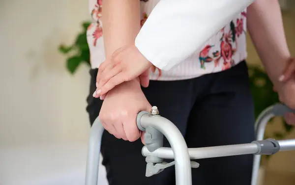 Doktor hastanın elini tutuyor, hareket etmesine yardım ediyor. Yetişkinler için aylaklar. Felç üstüne rehabilitasyon. Hastanede fizyoterapi. Ellerin görüntüsünü kapat..