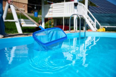 Genç kadın yüzme havuzu temizliyor. Güneşli yaz günlerinde havuzu yapraklardan temizleyen personel. Otel çalışanı havuzu temizliyor. Yüzme havuzu servisi. Ağ ile arındırma. Kapat.