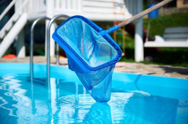 Genç kadın yüzme havuzu temizliyor. Güneşli yaz günlerinde havuzu yapraklardan temizleyen personel. Otel çalışanı havuzu temizliyor. Yüzme havuzu servisi. Ağ ile arındırma. Kapat.