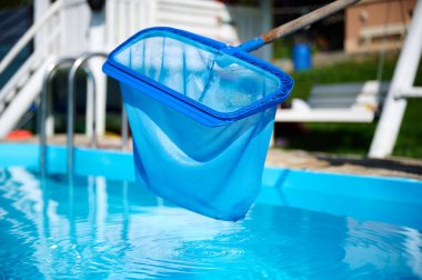 Genç kadın yüzme havuzu temizliyor. Güneşli yaz günlerinde havuzu yapraklardan temizleyen personel. Otel çalışanı havuzu temizliyor. Yüzme havuzu servisi. Ağ ile arındırma. Kapat.