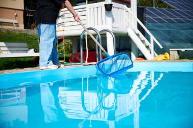 Genç kadın yüzme havuzu temizliyor. Güneşli yaz günlerinde havuzu yapraklardan temizleyen personel. Otel çalışanı havuzu temizliyor. Yüzme havuzu servisi. Ağ ile arıtma.