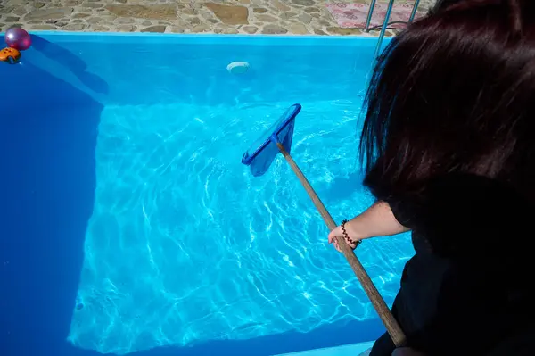 Enthusiastic cleaner ready to work. Young female holding cleaning equipment for swimming pools. Positive girl cleaning pool by pool skimmer.