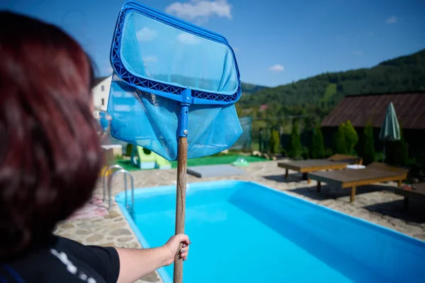 Young woman cleans swimming pool. Personnel cleaning the pool from leaves in sunny summer day. Hotel staff worker cleaning the pool. Cleaning swimming pool service. Purification with a net.