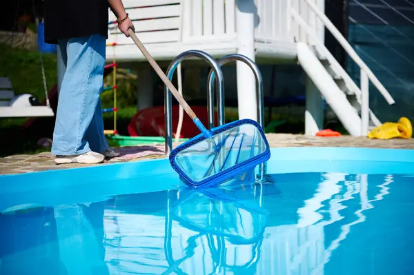 Enthusiastic cleaner ready to work. Young female holding cleaning equipment for swimming pools. Positive girl cleaning pool by pool skimmer.