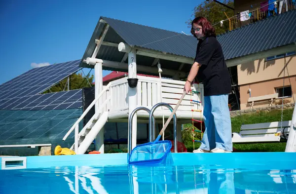 Young woman cleans swimming pool. Personnel cleaning the pool from leaves in sunny summer day. Hotel staff worker cleaning the pool. Cleaning swimming pool service. Purification with a net.