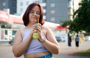 Güneşli bir günde limonata içen güzel bir kız. Genç bir kadın güneş ışığı yüzünden gözlerini kısıyor. Olumlu kız dışarıda içiyor ve dinleniyor..