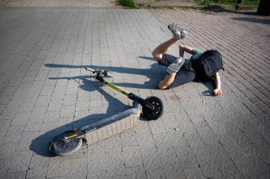 Dikkatsiz adam elektrikli scooter 'dan düştü. Genç erkek, araçtan düştükten sonra sırtüstü yatıyor. İlham perisi erkek bir arabaya çarpmış ve sırtını incitmiş..