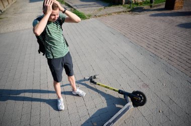 Dikkatsiz adam elektrikli scooter 'dan düştü. Aracından düştükten sonra kırık bir elektrikli scooter 'ın yanında duran genç erkek. İlham perisi erkek bir arabaya çarpmış ve sırtını incitmiş.