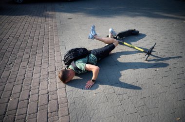 Dikkatsiz adam elektrikli scooter 'dan düştü. Genç erkek, araçtan düştükten sonra sırtüstü yatıyor. İlham perisi erkek bir arabaya çarpmış ve sırtını incitmiş..