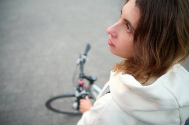 Sırt çantalı ve bisikletli bir kadının yakından çekilmiş portresi. Gün batımında setin içinde yürüyor. Üst görünüm.