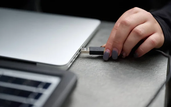 Closeup view of a girl plugging a USB plug into her laptop for charging from a portable solar panel. Female using portable solar panel to charge laptop and smartphone. Renewable energy. Cropped image