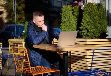 Genç, kendine güvenen iş adamı bir kafede oturuyor ve iş arkadaşları, akrabaları ya da arkadaşlarıyla çevrimiçi bir toplantıda dizüstü bilgisayardaki kameraya gülümsüyor.