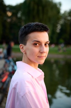 Genç kısa saçlı kız gün batımında bir iskelede oturuyor. Günlük giysiler içinde güzel bir kadın açık havada hayatın tadını çıkarıyor. Kentsel alanda yeşil bölge. Portreyi kapat.