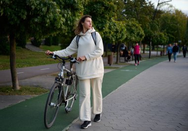 Sırt çantalı ve bisikletli bir kadının yakın plan portresi. Gün batımında setin içinde yürüyor..