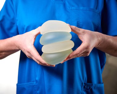 Kadın estetik cerrahın yakın çekimi yeni göğüsleri için bir hastaya göğüs implantı gösteriyor. Plastik cerrah göğüs silikonu takıyor. Göğüs büyütme konsepti. Göğüs implantı örnekleri