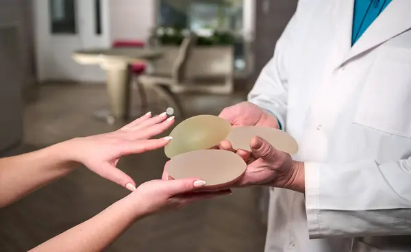 Kadın estetik cerrahın yakın çekimi yeni göğüsleri için bir hastaya göğüs implantı gösteriyor. Plastik cerrah göğüs silikonu takıyor. Göğüs büyütme konsepti. Göğüs implantı örnekleri