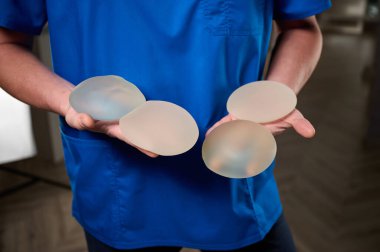 Kadın estetik cerrahın yakın çekimi yeni göğüsleri için bir hastaya göğüs implantı gösteriyor. Plastik cerrah göğüs silikonu takıyor. Göğüs büyütme konsepti. Göğüs implantı örnekleri