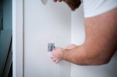 Elektrikçinin inşaat alanına tornavida kullanarak elektrik soketi kurduğu ekin manzarası. Güç soketi kurulumu. Duvardaki plastik bir kutuya elektrik prizi yerleştiriyorum..