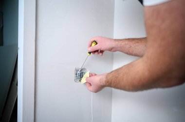 Elektrikçinin inşaat alanına tornavida kullanarak elektrik soketi kurduğu ekin manzarası. Güç soketi kurulumu. Duvardaki plastik bir kutuya elektrik prizi yerleştiriyorum..
