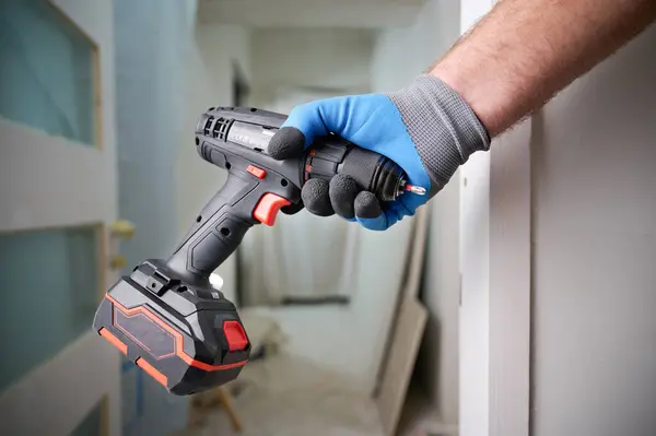 Construction worker holding electric cordless screwdriver in hand at construction site. Accessories for assembling, install furniture, repair home. Home renovation, electric tool for job. Crop view.
