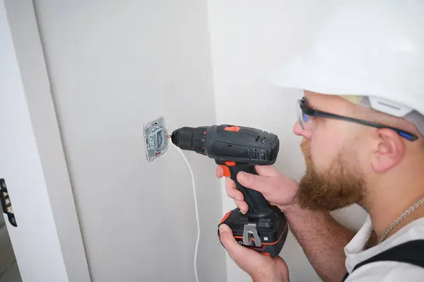 Crop view of electrician installing electric socket using screwdriver at construction site. Power socket installation. Installing a power outlet in to a plastic box on a wall.