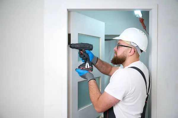Construction worker with a screwdriver installing a door. Accessories for assembling, install furniture, repair home. Man dressed in work attire, helmet and protective glasses. Home renovation concept