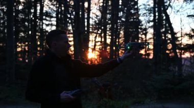 Güneşin doğuşunda dağlarda drone kontrolörü olan bir adam. İnsansız hava aracı pilotunun silueti dağlarda uçuyor. Yakın görünüm