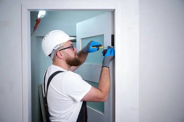 stock image Construction worker with a screwdriver installing a door. Accessories for assembling, install furniture, repair home. Man dressed in work attire, helmet and protective glasses. Home renovation concept