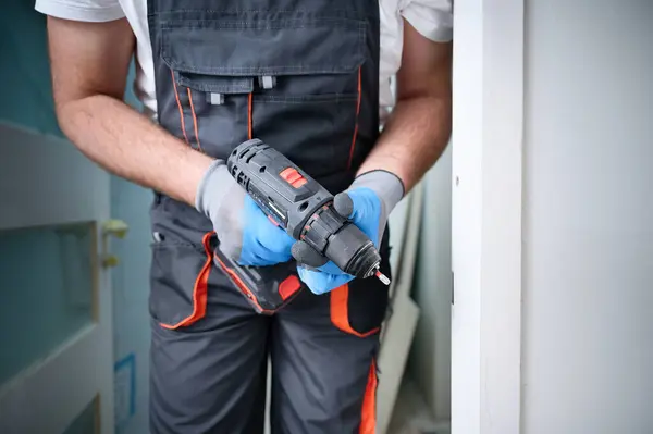 stock image Construction worker holding electric cordless screwdriver in hand at construction site. Accessories for assembling, install furniture, repair home. Home renovation, electric tool for job. Crop view.