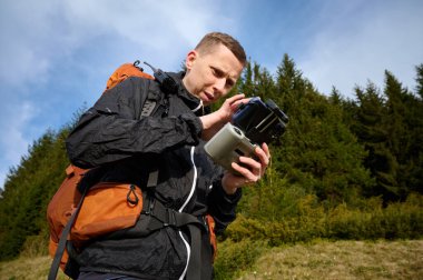 İHA operatörünün uzaktan kumandasını elinde tutarken yakın çekim görüntüsü. Gezgin, uzaktan kumandayla dağların üzerinden uçan bir dronu kontrol ediyor. Hava görüntüleme ve fotoğrafçılık.