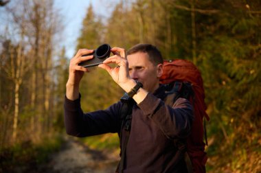 Tam donanımlı bir yürüyüşçü sabahın erken saatlerinde dağlarda akıllı telefondan gündoğumunun fotoğraflarını çekiyor. Cep telefonlu bir adam dağ yolunda güneşin doğuşunun tadını çıkarıyor. Görüntüyü kapat