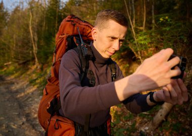 Tam donanımlı bir yürüyüşçü sabahın erken saatlerinde dağlarda akıllı telefondan gündoğumunun fotoğraflarını çekiyor. Cep telefonlu bir adam dağ yolunda güneşin doğuşunun tadını çıkarıyor. Görüntüyü kapat
