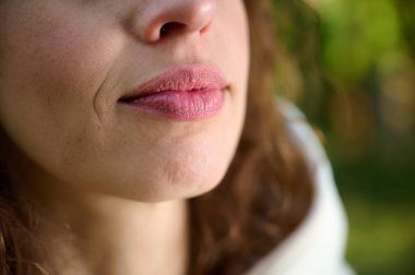 Kadın yüzü görüntüsü. Kırmızı dudaklı, gülümseyen esmer bir kızın portresi. Dudakların görüntüsünü kapat. Parkta yürüyen kadın..