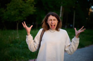 Hayal kırıklığına uğramış, şaşırmış, kızgın, şok olmuş, stresli, stresli, inançsız, bulanık arka planda hafif modern kapüşonlu bir kadın..