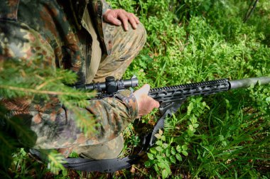 Tüfekli, kamuflaj kıyafetli avcı pusuda bekliyor. Ormanda pusuda bekleyen kamufle olmuş bir keskin nişancı. Askerler ormanda tüfekle saklanır..