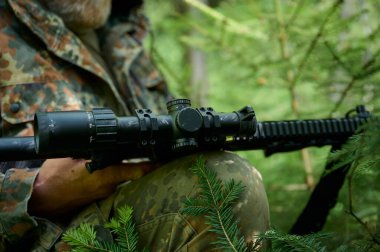 Tüfekli, kamuflaj kıyafetli avcı pusuda bekliyor. Ormanda pusuda bekleyen kamufle olmuş bir keskin nişancı. Askerler ormanda tüfekle saklanır..