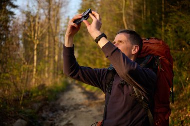 Tam donanımlı bir yürüyüşçü sabahın erken saatlerinde dağlarda akıllı telefondan gündoğumunun fotoğraflarını çekiyor. Cep telefonlu bir adam dağ yolunda güneşin doğuşunun tadını çıkarıyor. Görüntüyü kapat
