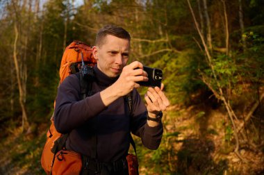 Tam donanımlı bir yürüyüşçü sabahın erken saatlerinde dağlarda akıllı telefondan gündoğumunun fotoğraflarını çekiyor. Cep telefonlu bir adam dağ yolunda güneşin doğuşunun tadını çıkarıyor. Görüntüyü kapat